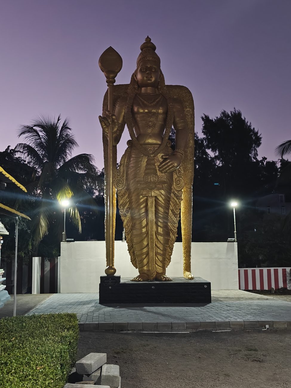 Une grande statue dorée d'un dieu tenant une lance, photographiée à la tombée de la nuit